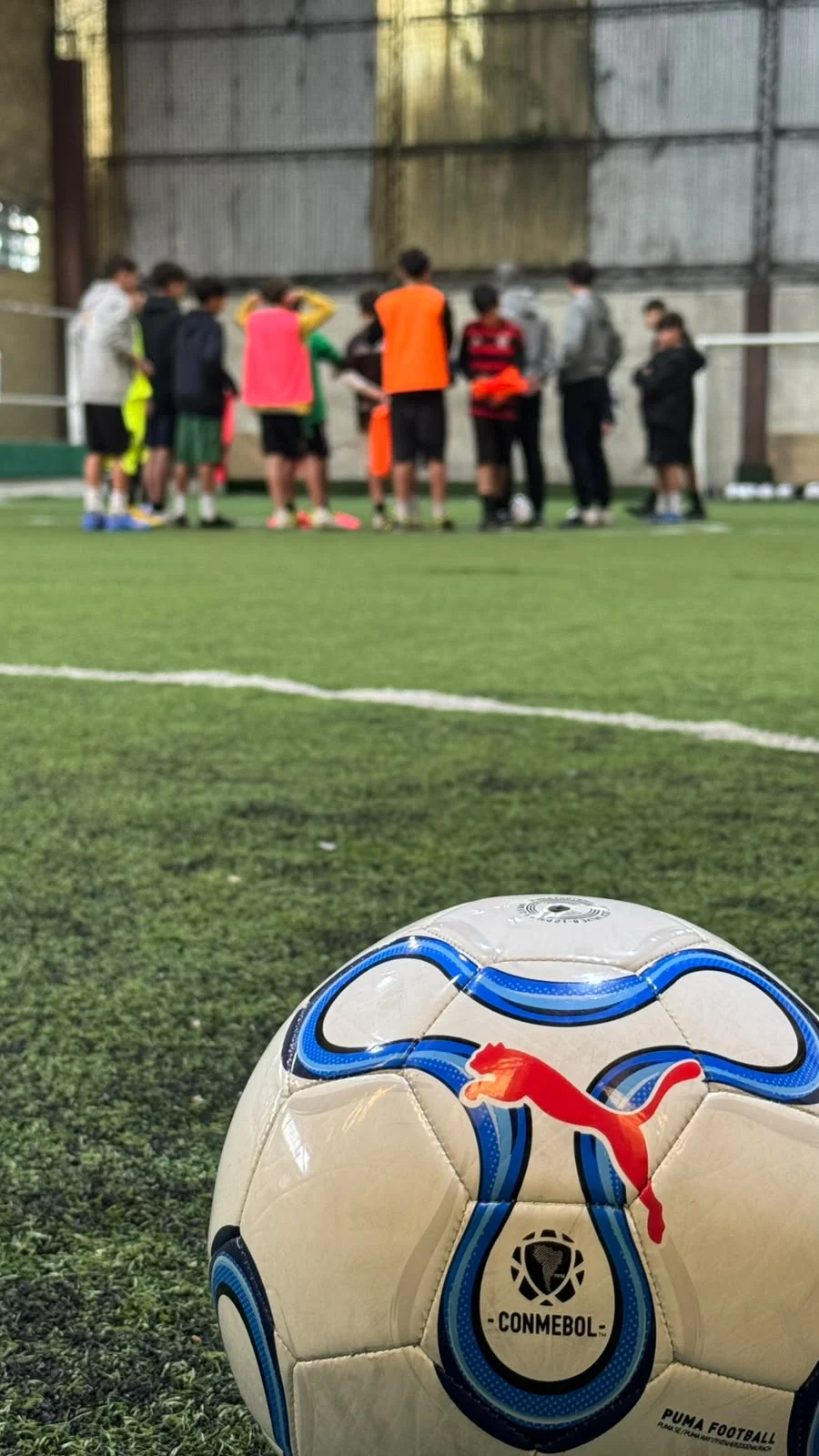 Balón Puma en primer plano con los jóvenes futbolistas y Facundo reunidos durante el entrenamiento